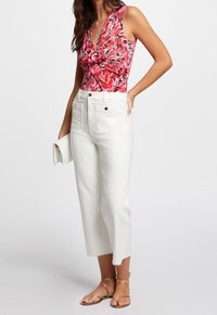 Bodysuit sin mangas con estampado floral en rojo y rosa, combinado con unos pantalones vaqueros de pierna ancha y cintura alta en blanco que presentan un dobladillo deshilachado y acentos de botón dorado.