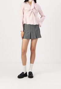Top di raso rosa con un fiocco al collo e motivo floreale, abbinato a una mini gonna plissettata grigia. Mocassini neri e calze bianche completano il look.