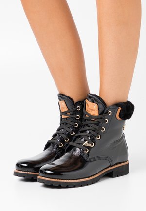 Botas de tobillo negras con cordones y acabado brillante, cuello de piel sintética, detalles de cuero y suela robusta. Presenta ojales dorados y marca.