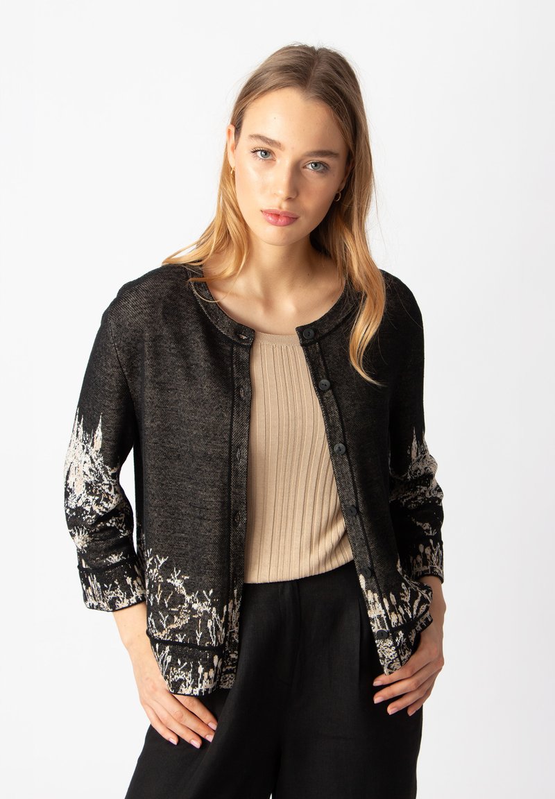 Čierne kardigán s bielou kvetinovou potlačou na rukávoch, okrúhly výstrih a gombíkový predný diel. Mäkká textúra, dlhé rukávy a voľný strih.