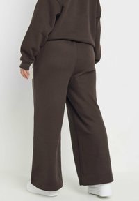 Bruna, löst sittande träningbyxor i mjuk tyg, med vida ben och elastisk midja, kombinerat med vita sneakers.