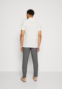 White short-sleeve shirt with perforated design, paired with gray tailored pants and light-colored shoes, viewed from the back.