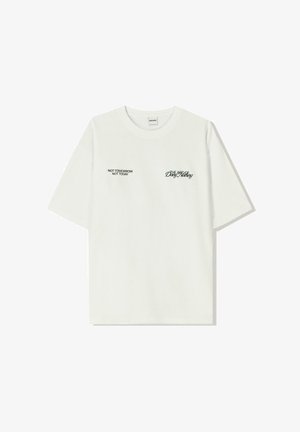 Fehér pamut póló rövid ujjakkal. Az elején fekete szöveg található: "NEM HOLNAP NEM MA" és "A FÖLD BŰVÉSZETE" zöld írással.