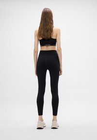 Fekete sportos crop top és magas derekú leggings, rugalmas anyagból, világos színű edzőcipővel párosítva, hátulról nézve.