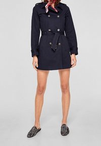 Granatowy trencz z podwójnymi guzikami, z paskiem w talii i naszywkami na ramionach. Połączony z butami slip-on w wzory.