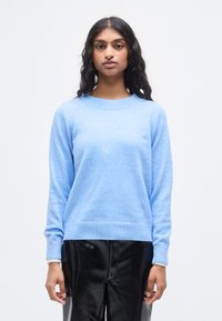 Ανοιχτό μπλε πουλόβερ από μαλακό, υφασμάτινο ύφασμα με υφή. Διαθέτει στρογγυλή λαιμόκοψη, ριμπ μανσέτες και τελείωμα, συνδυασμένο με λαμπερό μαύρο παντελόνι από ψεύτικο δέρμα.