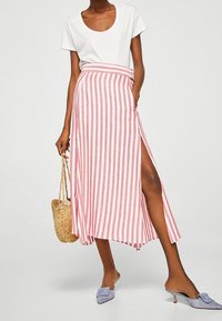 Jupe longue rayée rose et blanche avec une fente sur le côté, faite en tissu léger. Associée à un haut blanc et des chaussures bleues à enfiler.