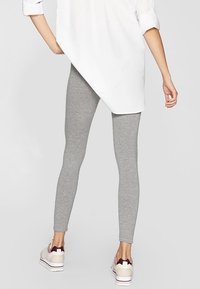 Leggings gris en coton extensible, offrant un ajustement près du corps. Portés avec une longue chemise blanche et des baskets multicolores.
