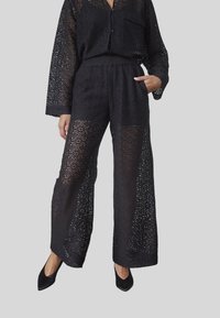 Sæti i sort guipure blonder bestående af en langærmet skjorte med knaplukning og vide bukser, der fremhæver indviklede mønstre og en gennemsigtig tekstur.