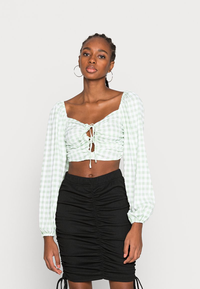 Top cropped em gingham verde e branco com mangas bufantes e detalhe de laço na frente, combinado com uma mini saia preta franzida.