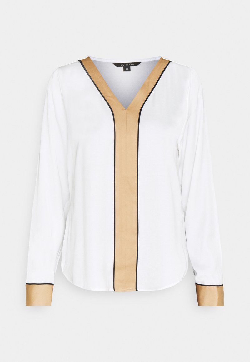 Blouse blanche à manches longues avec un bord en V beige s'étendant sur le devant et des poignets beiges, soulignés d'un fin passepoil noir.