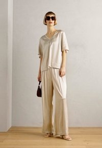 Light beige, silky V-neck top and wide-leg pants. Textured fabric with a smooth finish. Accented with dark sunglasses and a small brown bag.