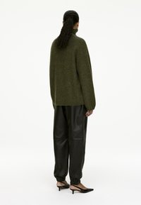 Oversized olive green sweater with high collar, paired with black leather jogger pants and black slingback heels. Smooth textures and relaxed fit.