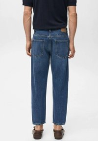 Jeans din denim albastru cu o croială dreaptă, având două buzunare la spate și o etichetă pe talie. Țesătura are o textură și un aspect clasic.