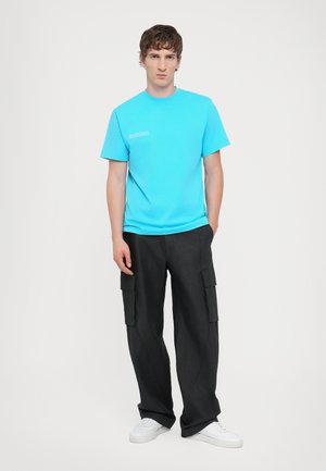 Turquoise cotton t-shirt with short sleeves, paired with black cargo pants featuring side pockets and white sneakers.