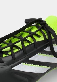 Crne i neon zelene sportske cipele s teksturiranim gornjim dijelom, crnim vezicama i bijelim akcentima. Ima tri uglasta pruge sa strane.