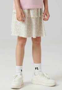 Gonna a balze floreale in colori pastello con una sensazione di consistenza. Indossata con sneakers bianche e calze a coste. Presenta più strati e balze.