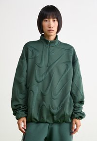 Πράσινο pullover sweatshirt με τέταρτο φερμουάρ, με ανάγλυφο σχέδιο λογότυπου Nike, φτιαγμένο από λείο ύφασμα, με ελαστικούς καρπούς και χαλαρή εφαρμογή.