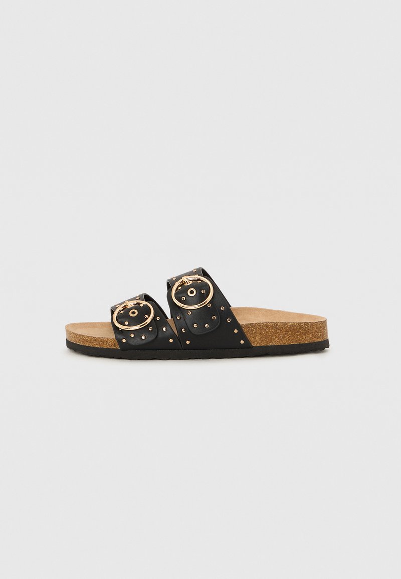 Sandales noires à glissière avec deux larges sangles comportant des boucles circulaires dorées, des accents cloutés et une semelle en liège. Semelle en caoutchouc texturé.