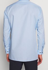 Lichtblauwe blouse met lange mouwen van gladde stof. Bevat een spread collar, knoopmanchetten met zwarte knopen en een rechte zoom.