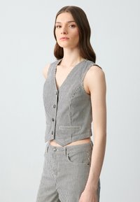 Top a righe cropped in bianco e nero, realizzato in tessuto tessuto, con scollatura profonda a V, cinque bottoni e due tasche frontali.