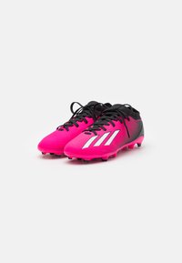 Scarpette da calcio rosa con una tomaia in mesh testurizzato, dotate di accenti neri e tre strisce bianche, progettate per offrire trazione su superfici erbose.