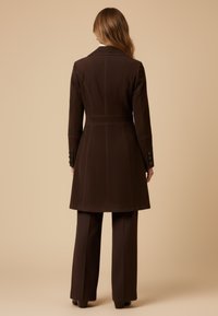 Brown fitted coat with a tailored silhouette, single-breasted design, and button details on sleeves, worn over matching brown pants.
