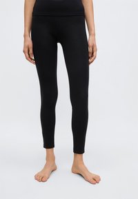 Leggings noirs en tissu lisse et extensible ; coupe ajustée avec taille mi-haute ; longueur cheville et ourlet sans couture.