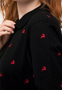 Polo noir avec un tissu texturé, arborant de petits motifs de rennes rouges, et un col noir côtelé.