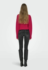 Maglione fucsia a maglia, design cropped, jeans skinny neri abbinati a stivali neri alti fino al ginocchio con tacco chunky, visti da dietro.