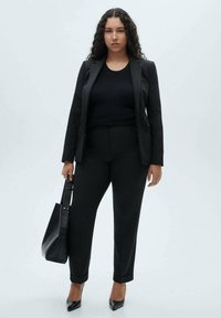 Black suit featuring a tailored blazer and fitted trousers, paired with a black ribbed top and a structured black handbag. High-heeled shoes.