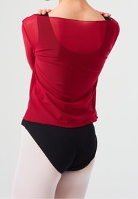 Rode mesh top met een off-shoulder ontwerp en zwarte banden, gecombineerd met zwarte dansshorts en lichtroze panty's.