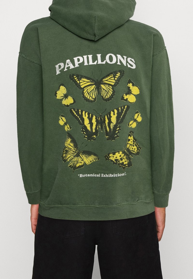 Zelená mikina s kapucí, na které je grafika motýla v žluté a černé barvě, s texty "PAPILLONS" a "Botanická výstava" níže. Bavlněná látka.