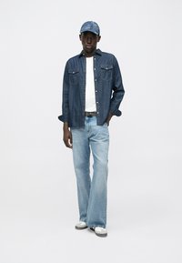 Tamsiai mėlyna džinsinė marškinėliai su dviem kišenėmis ant krūtinės, derinami su šviesiai mėlynomis išplatintomis džinsų kelnėmis ir derančia džinsine kepure. Avalynė su pilkomis detalėmis.