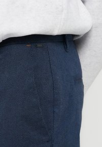 Κοντινό πλάνο στη μέση και την τσέπη μπλε παντελονιού με υφή, σε συνδυασμό με ανοιχτό γκρι φούτερ που έχει μπει μέσα.