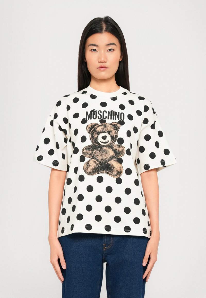 White short-sleeve T-shirt with black polka dots, featuring a teddy bear graphic and "MOSCHINO" text in bold black letters.