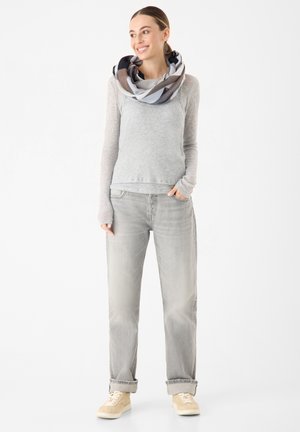 Haut gris à manches longues, jean gris clair et baskets beiges. Une écharpe à motifs drape autour du cou. Textures douces et coupe décontractée.