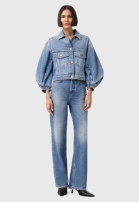 Giacca di denim cropped con maniche a palloncino, colore azzurro chiaro, chiusura frontale con bottoni, e due tasche sul petto; abbinata a jeans a gamba dritta.