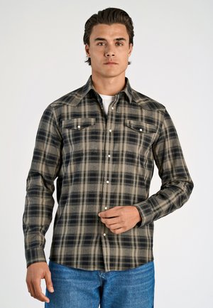 Geruite flanellen overhemd in grijs, zwart en beige. Heeft een knoopsluiting aan de voorkant, twee borstzakken en een kraag. G gedragen met blauwe jeans.