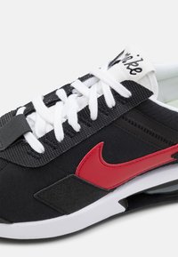 Černé tenisky s červeným logem Nike, bílými tkaničkami a texturovaným svrškem. Obsahují bílou mezipodešev a černou podešev pro kontrast.