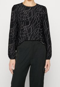 Blusa nera a maniche lunghe con un motivo ondulato argento, scollatura rotonda e polsini elasticizzati, abbinata a pantaloni neri a vita alta.