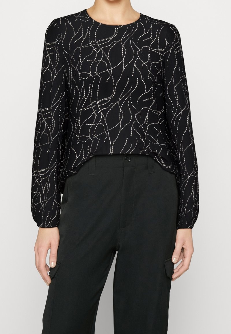 Blusa nera a maniche lunghe con un motivo ondulato argento, scollatura rotonda e polsini elasticizzati, abbinata a pantaloni neri a vita alta.