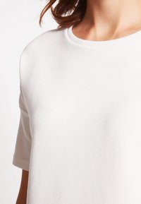 Vit kortärmad topp med ribbad struktur, rund hals och mjukt tyg. Designen har en avslappnad passform och minimal detaljer.