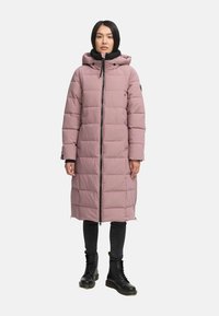 Lyserød pufferjakke med hætte, quiltet tekstur, lynlås foran og sidelommer. Kombineret med sorte jeans og kampstøvler.