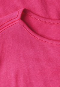 Tejido de algodón de un brillante color rosa, con una textura suave, que presenta un escote redondeado y costuras en contraste a lo largo de los bordes.