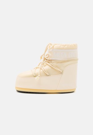 Botte de lune beige clair avec un bout rond, une fermeture à cordon de serrage et une semelle en caoutchouc texturé. Comprend un logo blanc et des matériaux synthétiques lisses.