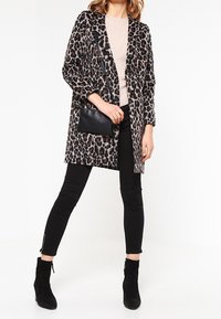 Leopardmönstrad kappa med avslappnad passform, långa ärmar och en framficka, kombinerad med svarta leggings och ankelskor. Mjukt, texturerat tyg.