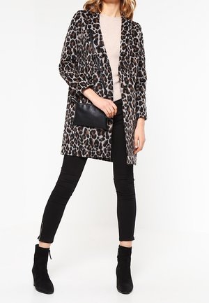 Płaszcz w panterkę o luźnym kroju, z długimi rękawami i kieszenią z przodu, zestawiony z czarnymi legginsami oraz botkami za kostkę. Miękka, teksturowana tkanina.