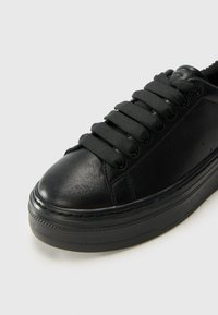 Sneaker in pelle nera con lacci neri piatti, punta arrotondata, pannellatura testurizzata e una suola in gomma spessa con un sottile motivo di battistrada.