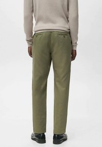 Pantalones verdes oliva con una textura suave, diseño ajustado, bolsillos laterales y traseros, combinados con un suéter de canalé beige claro y zapatos negros.